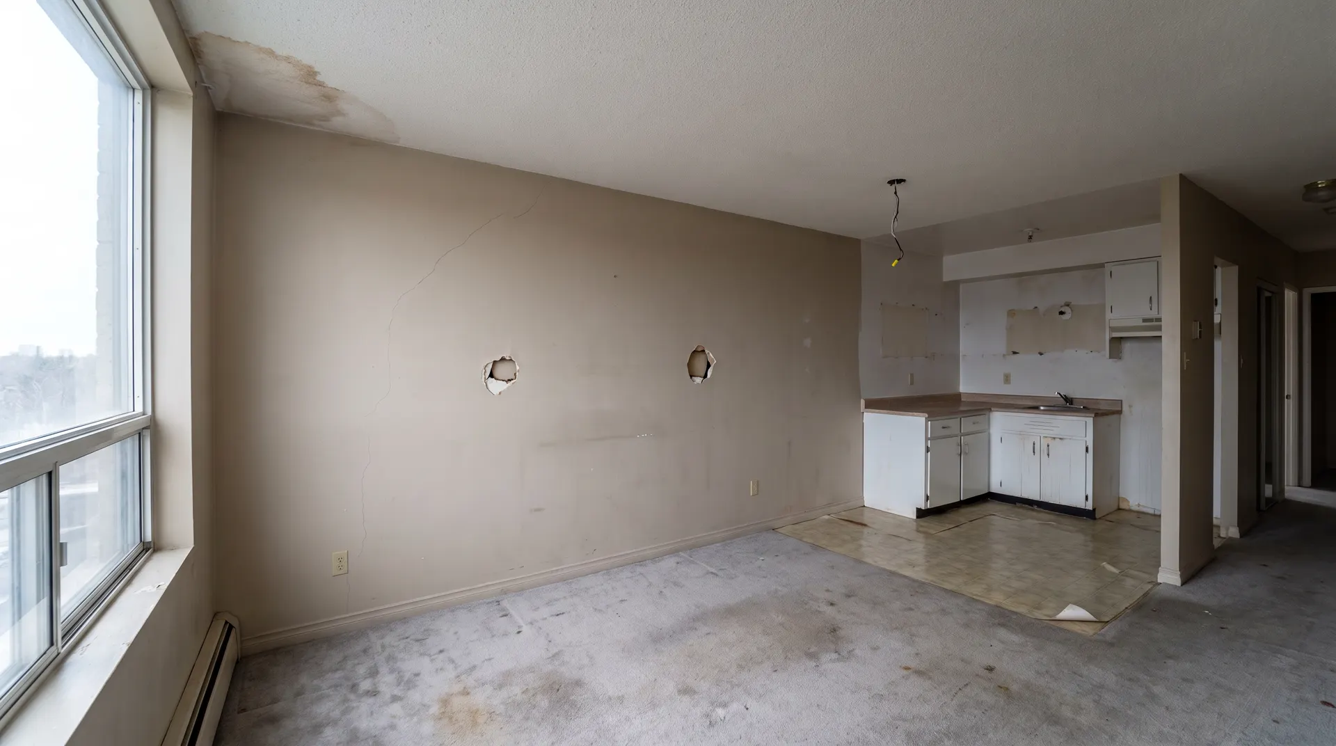 Illustration of an empty apartment unit at turnover, with holes and a crack in the drywall, a stained ceiling and worn carpet